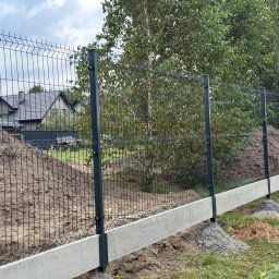 Kermit Ogrodzenia Piotr Sałański - Nowo zamontowane ogrodzenie z siatki panelowej na betonowej podmurówce, widoczne słupki i fragment domu w tle, na trawie pozostałości po pracach ziemnych.