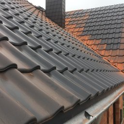 K-ROMDACH - Ciemna dachówka ceramiczna na skośnym dachu z widocznym kominem i rynną. Część dachu pokryta starą, pomarańczową dachówką. Widok z góry na fragment dachu.