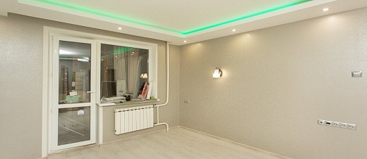 Wykończone wnętrze pokoju z szarą tapetą, białymi drzwiami balkonowymi i grzejnikiem. Sufit z zielonym oświetleniem LED. Nowoczesne gniazdka elektryczne.