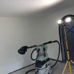 Woji SOLAR-TECH - Pokój w trakcie prac szpachlarskich: szlifierka z odkurzaczem Festool, lampa oświetleniowa, ściany po szpachlowaniu, przygotowane do malowania.