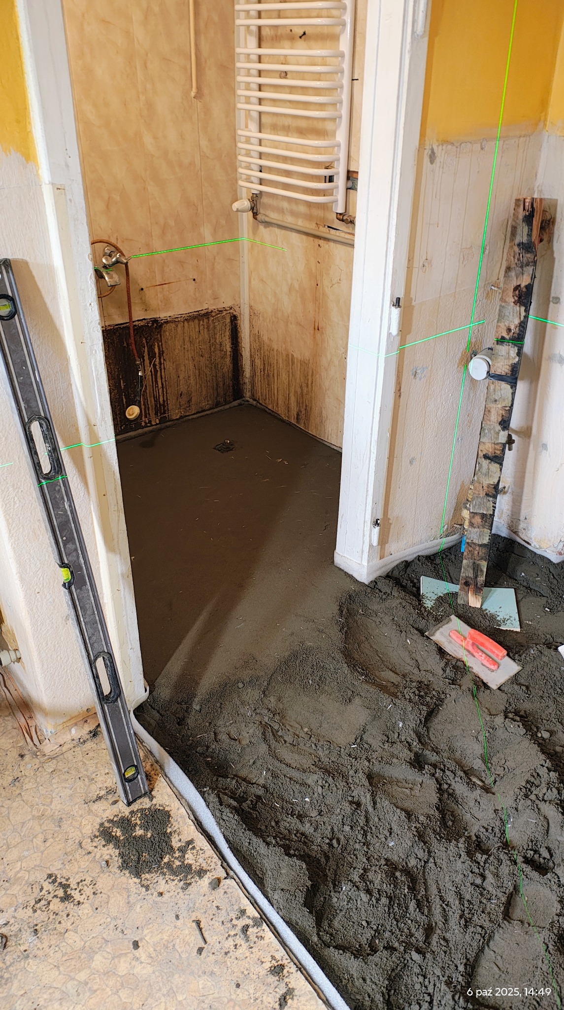 Wyrównywanie podłoża w łazience z użyciem poziomicy laserowej. Widoczne narzędzia i fragmenty starej instalacji, przygotowanie do dalszych prac wykończeniowych.