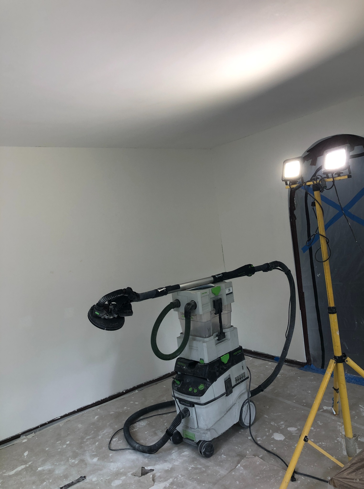 Pokój w trakcie prac szpachlarskich: szlifierka z odkurzaczem Festool, lampa oświetleniowa, ściany po szpachlowaniu, przygotowane do malowania.