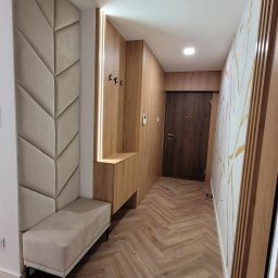 Klemba Design - Nowoczesny przedpokój z tapicerowanym panelem ściennym w kształcie jodełki, drewnianą zabudową z wieszakami i siedziskiem oraz podłogą ułożoną w jodełkę.
