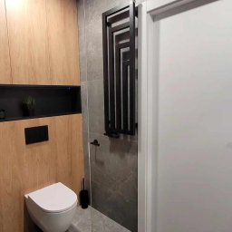 Klemba Design - Nowoczesna łazienka z drewnianą zabudową, szarą płytką i czarnym grzejnikiem drabinkowym. Wisząca toaleta i minimalistyczne dodatki.