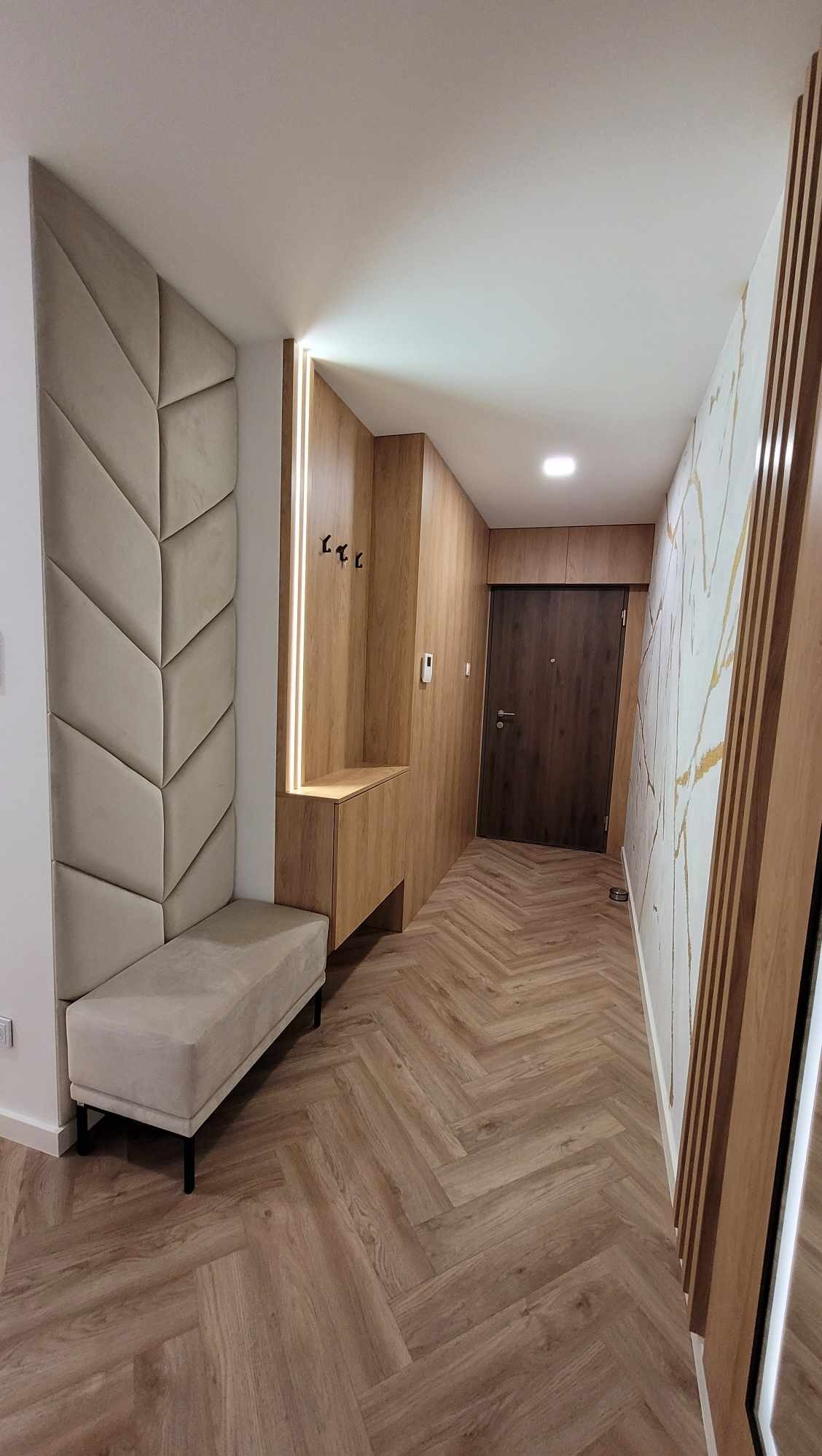 Nowoczesny przedpokój z tapicerowanym panelem ściennym w kształcie jodełki, drewnianą zabudową z wieszakami i siedziskiem oraz podłogą ułożoną w jodełkę.