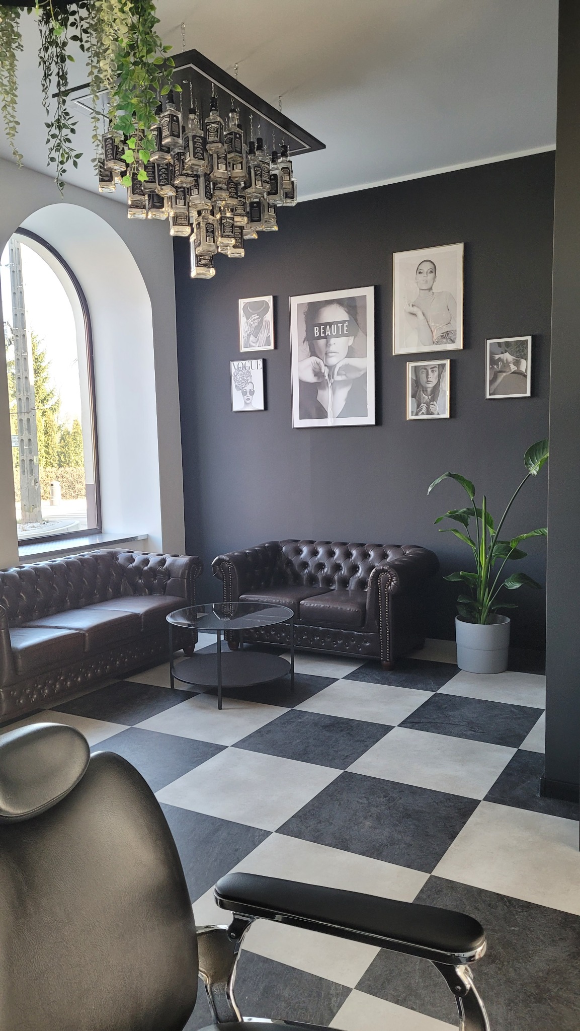Stylowa poczekalnia z fotelami chesterfield i szachownicą na podłodze w Rawie Mazowieckiej. Oryginalny żyrandol z butelek Jack Daniel's.