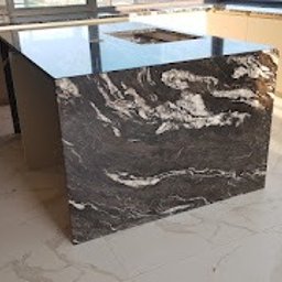 Orpol Sp.z o.o. - Wyspa kuchenna z blatem z czarnego kamienia z białymi żyłami, odbijająca światło, na tle jasnych płytek podłogowych i zabudowy kuchennej.