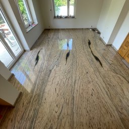 Orpol Sp.z o.o. - Polerowana posadzka z kamienia naturalnego w jasnych odcieniach beżu i brązu, z wyraźnym, unikalnym wzorem żyłkowania. Widok z góry, okna w tle.