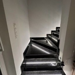 Orpol Sp.z o.o. - Nowoczesne schody z czarnego kamienia z subtelnym podświetleniem LED, widok z dołu. Minimalistyczny design, gładka powierzchnia, eleganckie wykończenie.