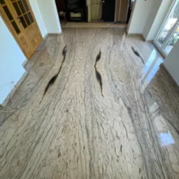 Polerowana podłoga z kamienia naturalnego o unikalnym wzorze żyłkowania, ułożona w jasnym wnętrzu z widocznymi drzwiami i oknami. Perspektywa z góry.