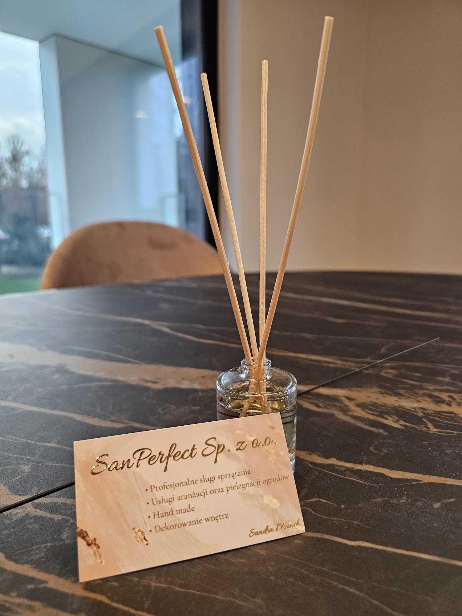 Aromatyzer z logo firmy San Perfect Sp. z o.o. oferującej usługi sprzątania, aranżacji ogrodów, rękodzieła i dekoracji wnętrz, na marmurowym stole.