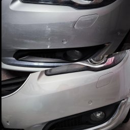 Rafal Trembinski - Zestawienie stanu przed i po lakierowaniu: zarysowany, srebrny zderzak samochodu po naprawie prezentuje się gładko i lśniąco. Widoczna lampa i fragment grilla.