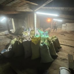 Robimy Robotę ROBERT BALCERAK - Wnętrze poddasza z workami gruzu i pracownikiem w tle, przygotowane do wywozu po remoncie. Widoczne narzędzia i prowizoryczne oświetlenie.