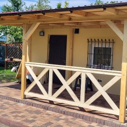 INSTAL-WOOD WIESŁAW SZWED - Drewniana altana z beżową elewacją i dekoracyjną balustradą w kształcie litery X, otoczona zielenią ogrodu i kolorowymi kwiatami w donicach.