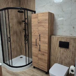 INSTAL-WOOD WIESŁAW SZWED - Nowoczesna łazienka po remoncie: kabina prysznicowa z czarnymi profilami, drewnopodobne panele ścienne, szafka i toaleta. Oświetlenie sufitowe.