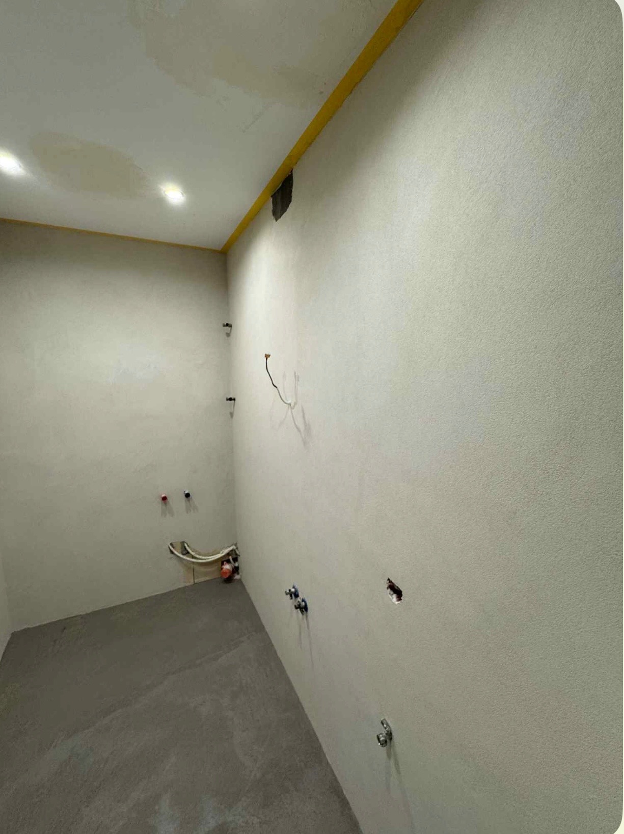 Przygotowana do wykończenia łazienka: szpachlowane ściany, wylewka, wyprowadzone instalacje wod-kan i elektryczne, żółta taśma zabezpieczająca pod sufitem.