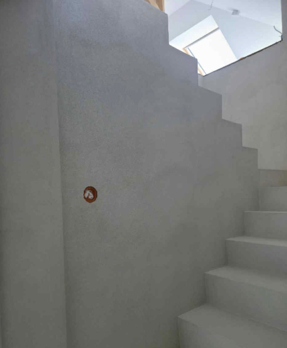 Schody wewnątrz budynku po szpachlowaniu i malowaniu na biało, widoczne gładkie ściany i okno dachowe. Minimalistyczny design.