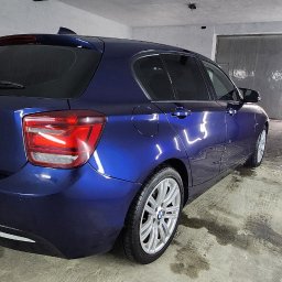 FENIX CENTRUM - Błyszczący, granatowy BMW serii 1 po detailingu, zaparkowany w garażu z widocznymi śladami opon na posadzce. Widok z tyłu, z lekkim kątem bocznym, ukazujący odnowiony lakier.