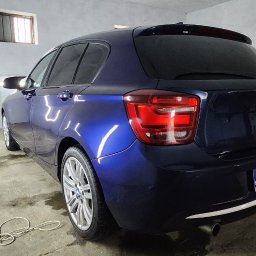 FENIX CENTRUM - Błyszczący, granatowy BMW hatchback po detailingu w garażu z lampami inspekcyjnymi; widoczny tylny zderzak, tablica rejestracyjna i felgi aluminiowe.