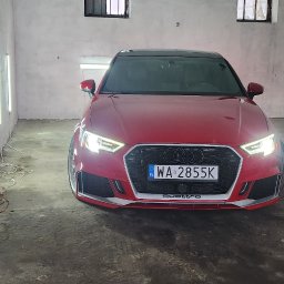 FENIX CENTRUM - Czerwone Audi A3 Quattro z włączonymi światłami, zaparkowane w garażu z lampami inspekcyjnymi. Widoczny numer rejestracyjny WA 2855K. Garaż z surowymi ścianami.