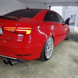 FENIX CENTRUM - Czerwone Audi A3 po tuningu, z widocznym spojlerem, felgami i podwójnym wydechem, sfotografowane w garażu z oświetleniem LED. Tablica rejestracyjna WA 2855K.