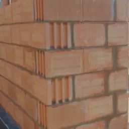 Fragment ściany z czerwonej ceramiki poryzowanej, widoczne spoiny i charakterystyczna struktura pustaków, budowa w toku.