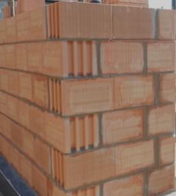 Fragment ściany z czerwonej ceramiki poryzowanej, widoczne spoiny i charakterystyczna struktura pustaków, budowa w toku.