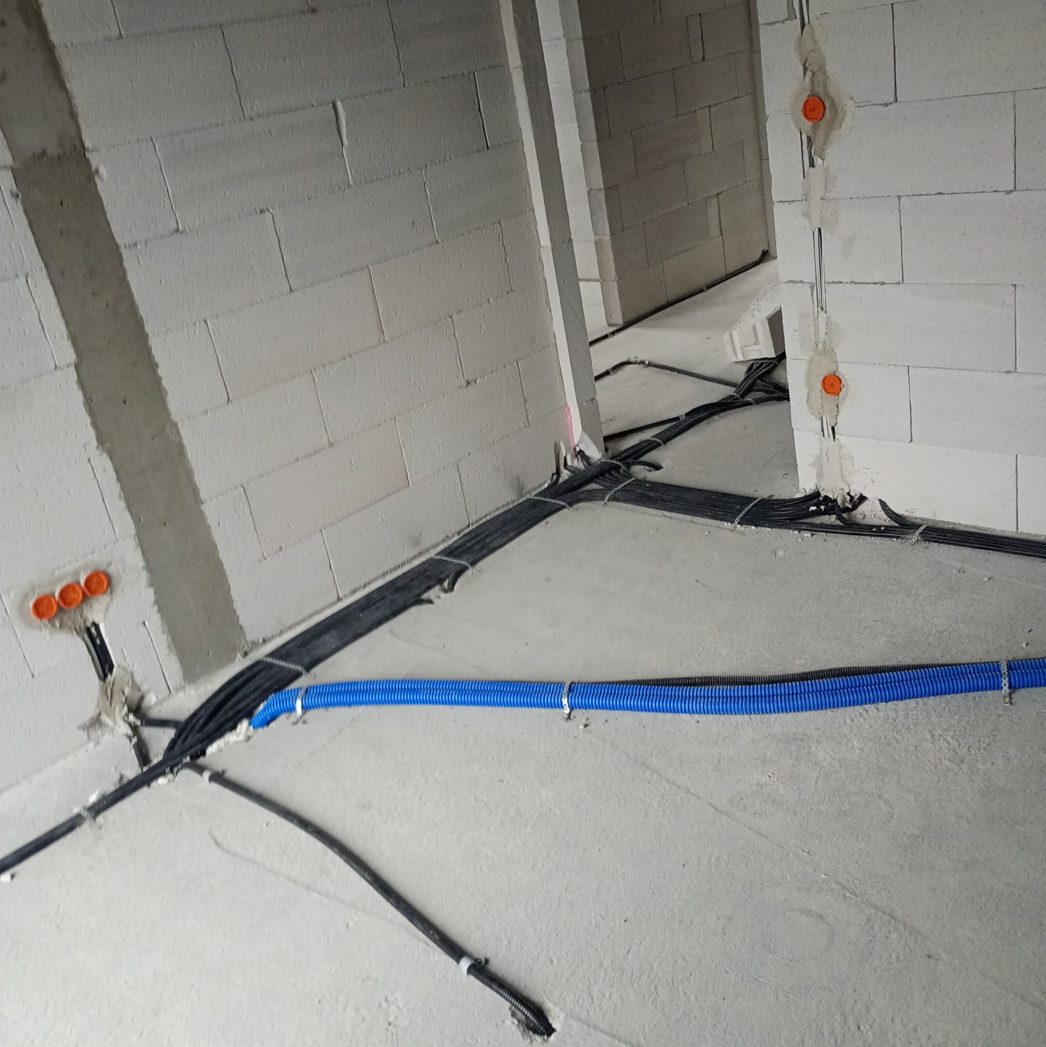 Instalacja elektryczna w surowym wnętrzu: kable w peszlach, puszki podtynkowe z pomarańczowymi dekielkami, ściany z betonu komórkowego. Etap prac przed tynkowaniem.