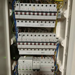 Michał Lisiecki - Rozdzielnia elektryczna z bezpiecznikami, przewody w różnych kolorach, listwy zaciskowe. Instalacja elektryczna wewnątrz obudowy. Widoczne zabezpieczenia przeciwprzepięciowe.