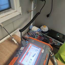 Michał Lisiecki - Miernik elektryczny Anel MPI-540 pokazuje impedancję pętli zwarcia ZL-N 1,327 Ω. W tle gniazdko elektryczne, okno i przedmioty leżące na stole.