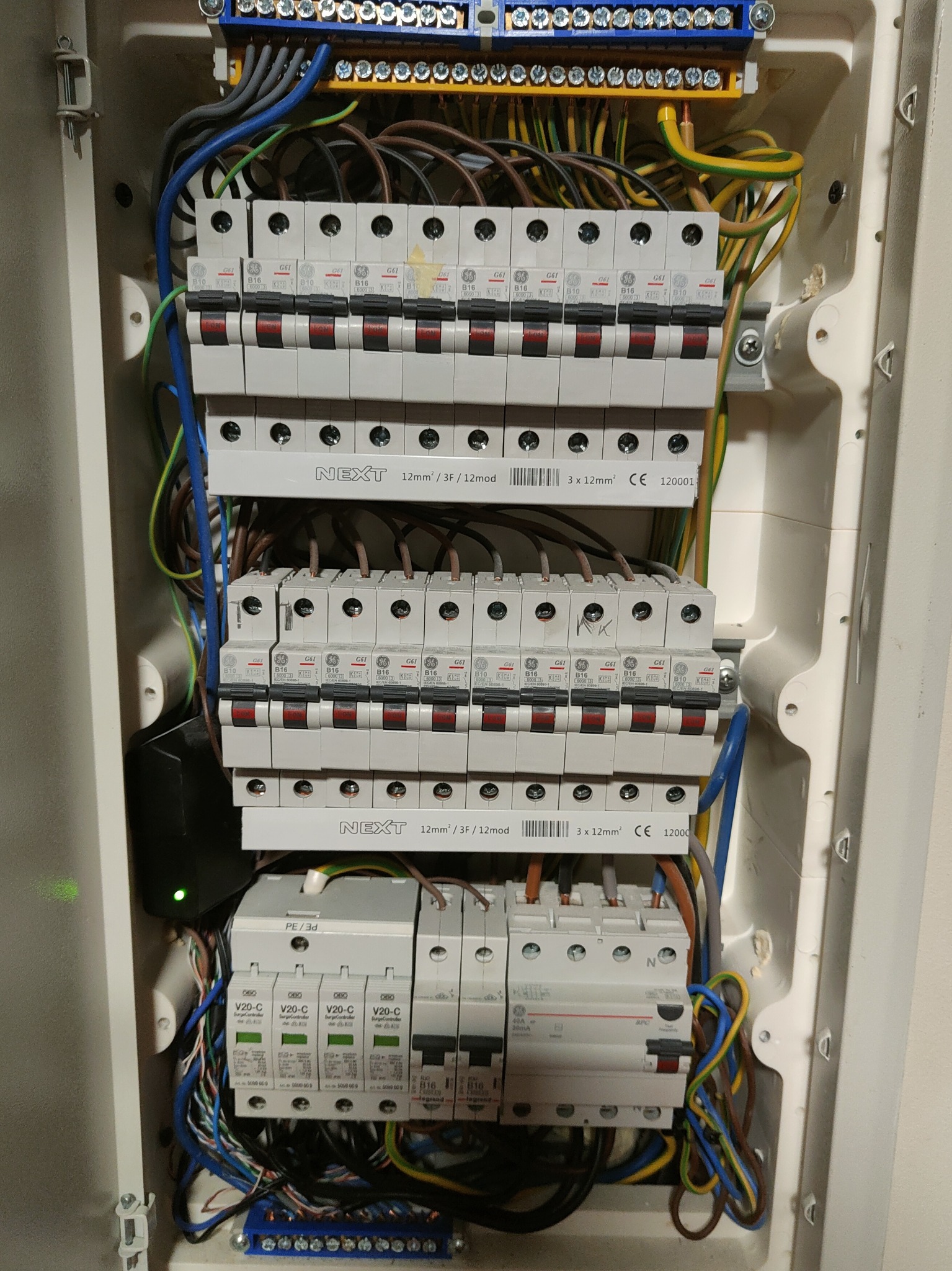 Rozdzielnia elektryczna z bezpiecznikami, przewody w różnych kolorach, listwy zaciskowe. Instalacja elektryczna wewnątrz obudowy. Widoczne zabezpieczenia przeciwprzepięciowe.