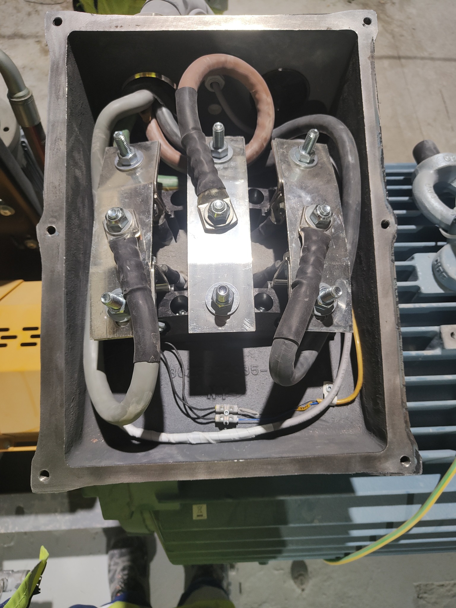 Złącze silnika elektrycznego z podłączonymi przewodami zasilającymi, widoczne śruby i nakrętki mocujące. Ujęcie z góry, detale instalacji.