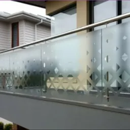 Balkon z matową szybą z geometrycznym wzorem rombów i stalową balustradą. Nowoczesny design, jasne tło budynku, widok z dołu na górę.