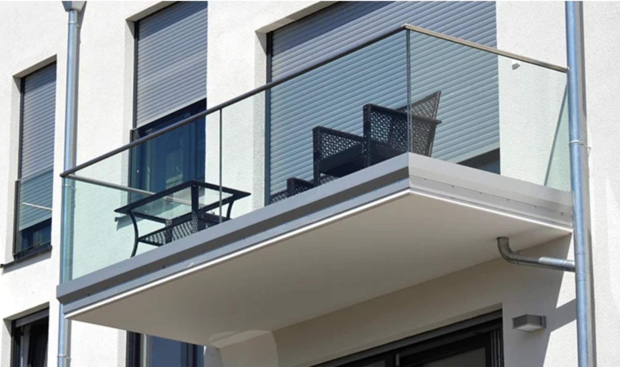Nowoczesny balkon z szklaną balustradą i czarnymi meblami rattanowymi. Okna z roletami. Minimalistyczny design.