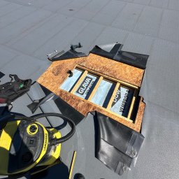 Piotr Nik - Naprawa dachu z papy: odsłonięta warstwa izolacyjna Glava i Dow Vepro, narzędzia, odkurzacz Karcher, buty dekarza. Widok z góry na płaski dach podczas prac.