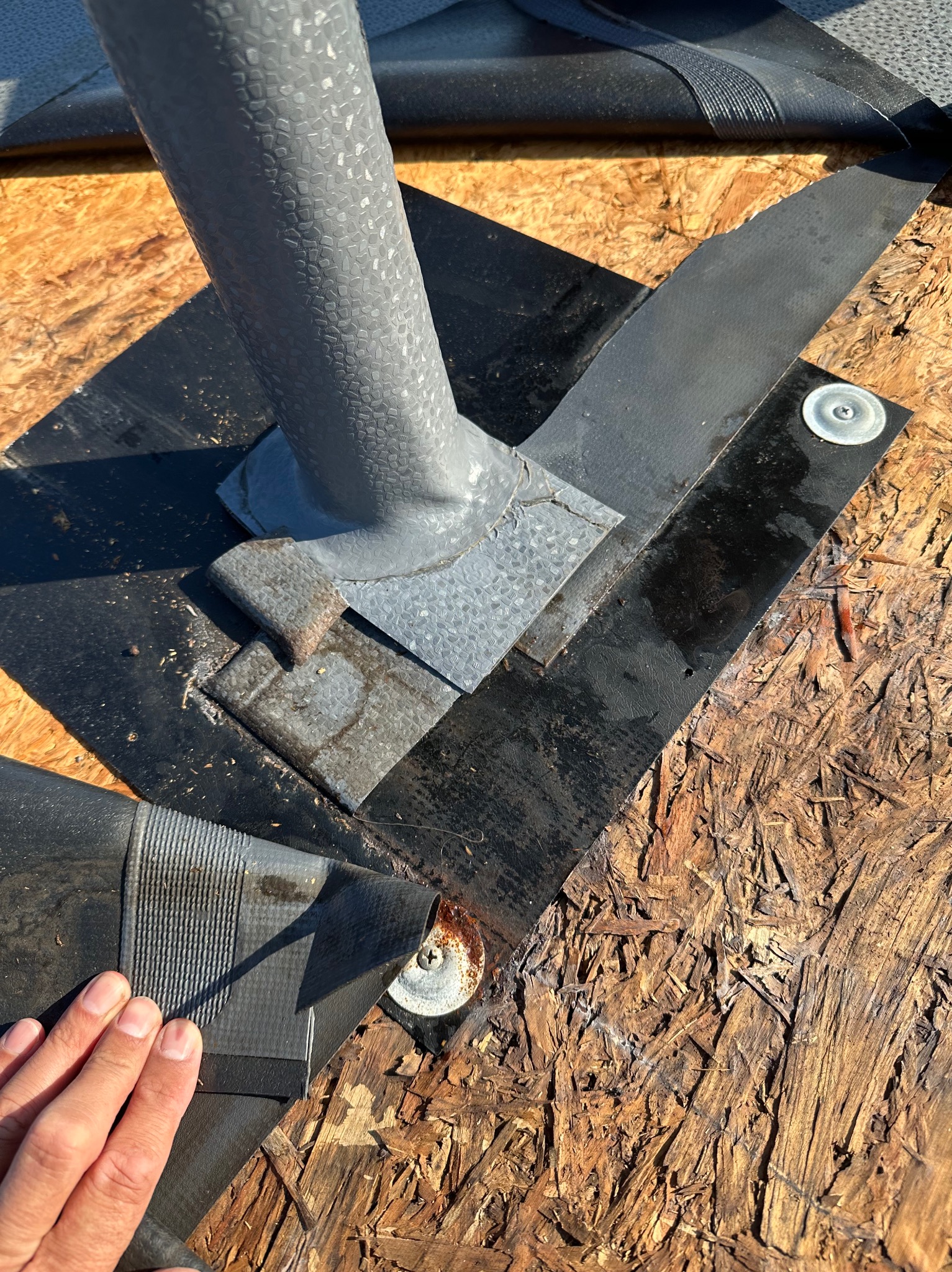 Szczegółowe ujęcie fragmentu dachu z zamontowaną obróbką komina i papą, widoczne elementy mocujące. Tekstura płyty OSB w tle.