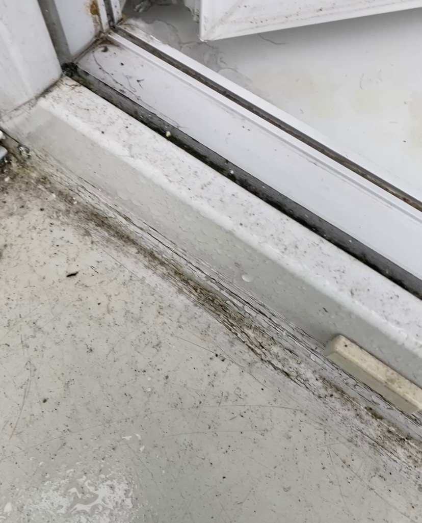 Zabrudzone, białe okno PCV z widocznymi smugami i plamami. Szczegółowe ujęcie na dolną ramę i parapet przed czyszczeniem, zarysowania i resztki po zalaniu.