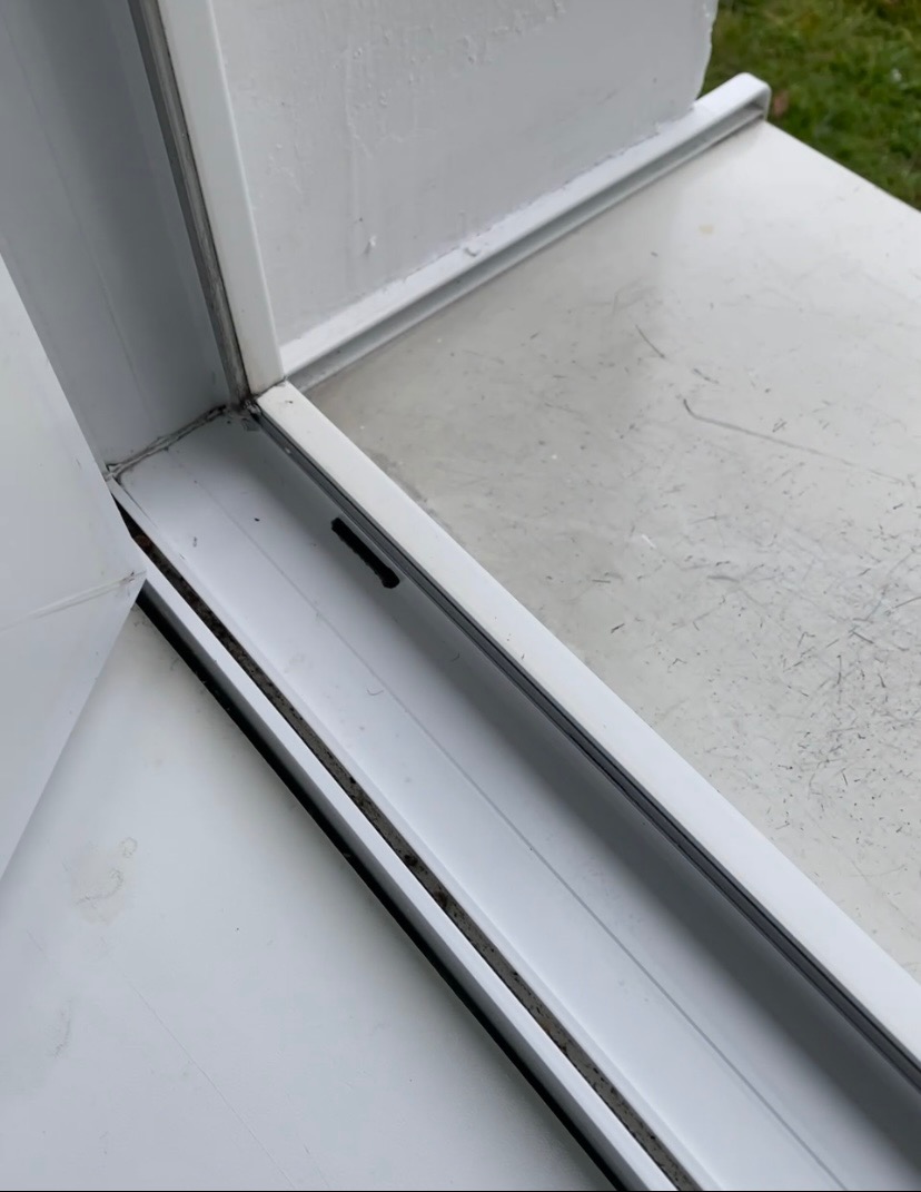 Szczegółowe ujęcie zabrudzonego, białego okna PCV w rogu, z widocznymi śladami pleśni i kurzu wzdłuż ramy i uszczelki, wymagającego dokładnego czyszczenia.