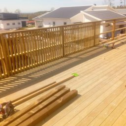 Holhauser - Jasna, drewniana balustrada tarasu w trakcie budowy, z widocznymi deskami, narzędziami i domem w tle. Słoneczny dzień, świeże drewno.