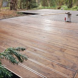 Holhauser - Impregnowana drewniana podłoga tarasu z widoczną puszką farby i pędzlem, podkreślająca detale wykończenia i estetykę. Częściowo pomalowana podłoga.