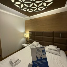Góralskie Sprzątanie - Czysty pokój hotelowy z broszurami 'Góralskie Sprzątanie' na łóżku. Dekoracyjna lampa sufitowa i starannie złożone ręczniki podkreślają dbałość o detale.