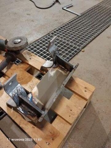 Element metalowy po spawaniu, szlifowany, leżący na palecie. W tle kratka ściekowa i narzędzia. Widoczne ślady obróbki i niedoskonałości materiału.