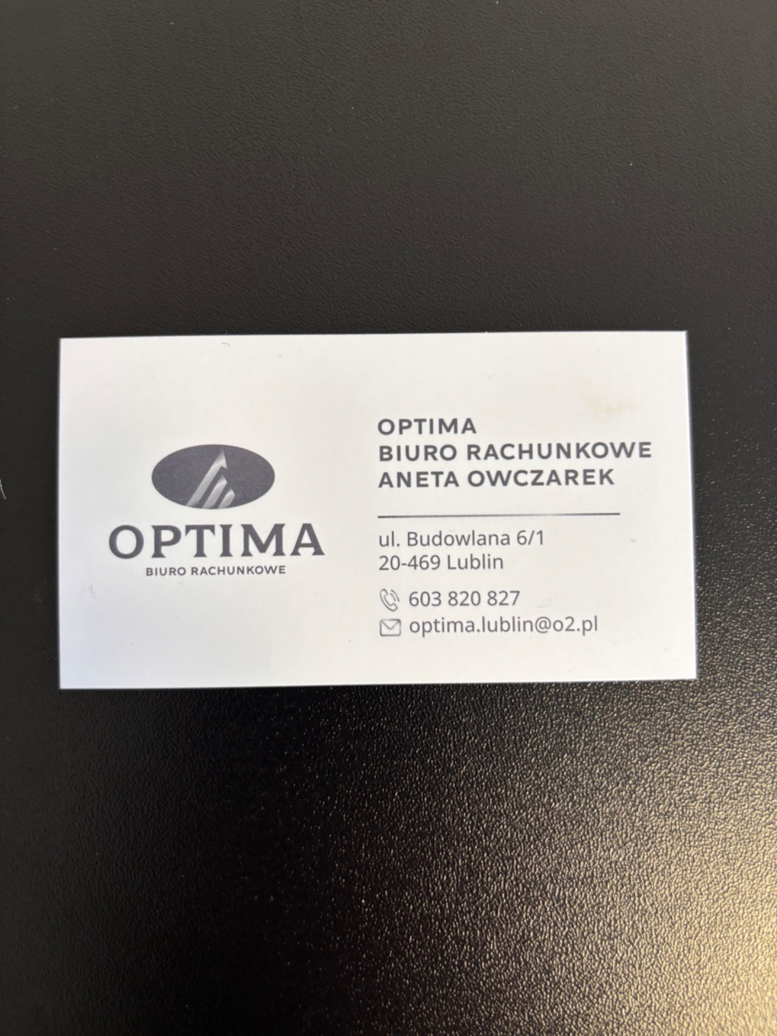 Wizytówka biura rachunkowego Optima Anety Owczarek z Lublina, z adresem ul. Budowlana 6/1 i danymi kontaktowymi. Minimalistyczny design na ciemnym tle.