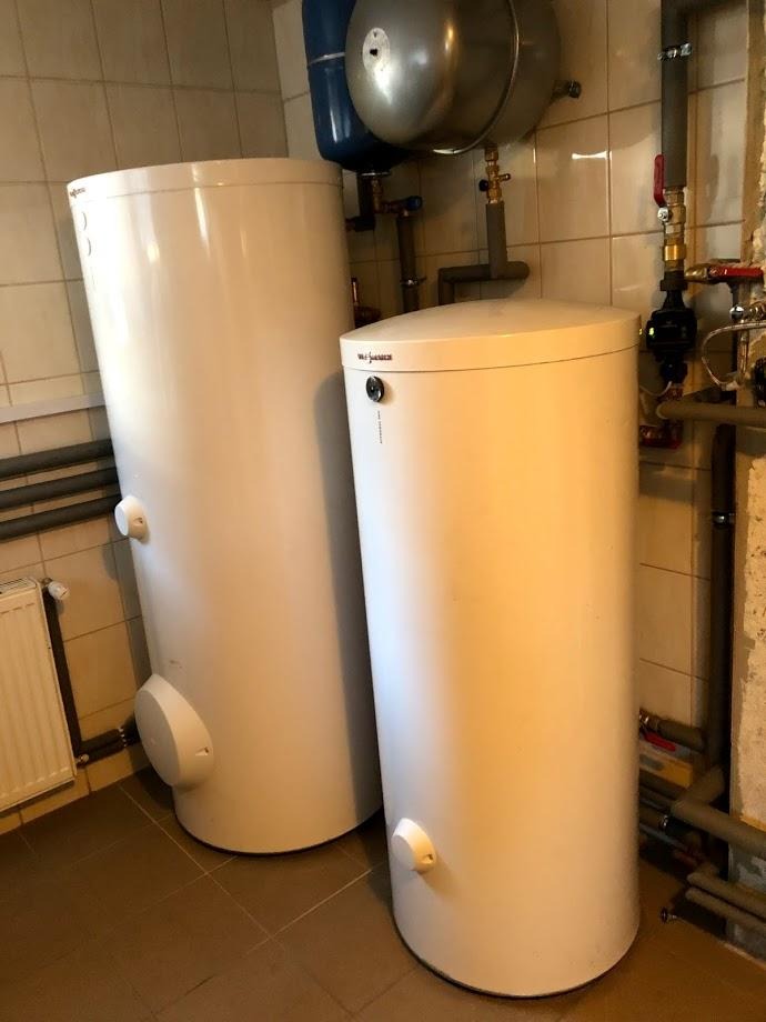 Dwa białe, cylindryczne zasobniki ciepłej wody użytkowej marki Viessmann w kotłowni, z widocznymi rurami i armaturą. Jasne płytki na ścianach i podłodze.