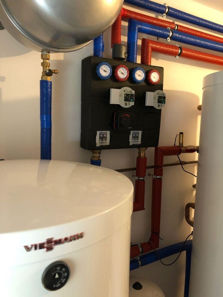 Instalacja grzewcza Viessmann: biały zbiornik, czarny panel sterowania z manometrami, czerwone i niebieskie rury. Elementy połączone, gotowe do użytku.