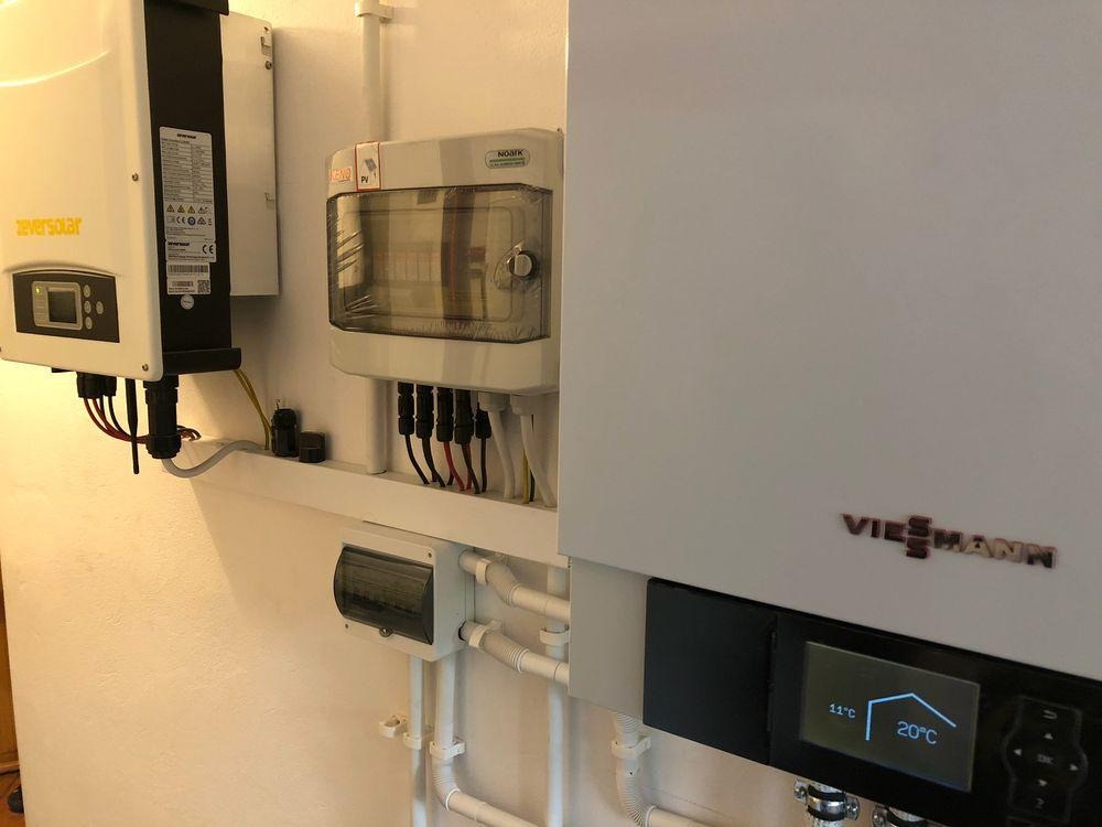 Biały piec Viessmann z wyświetlaczem, instalacja elektryczna, skrzynka rozdzielcza i inwerter Zeversolar na białej ścianie. Widoczne rury i kable.