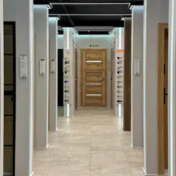 Salon z ekspozycją drzwi wewnętrznych różnych modeli, oświetlony ledami, z drewnianą okleiną i przeszkleniami, widok z perspektywy korytarza.