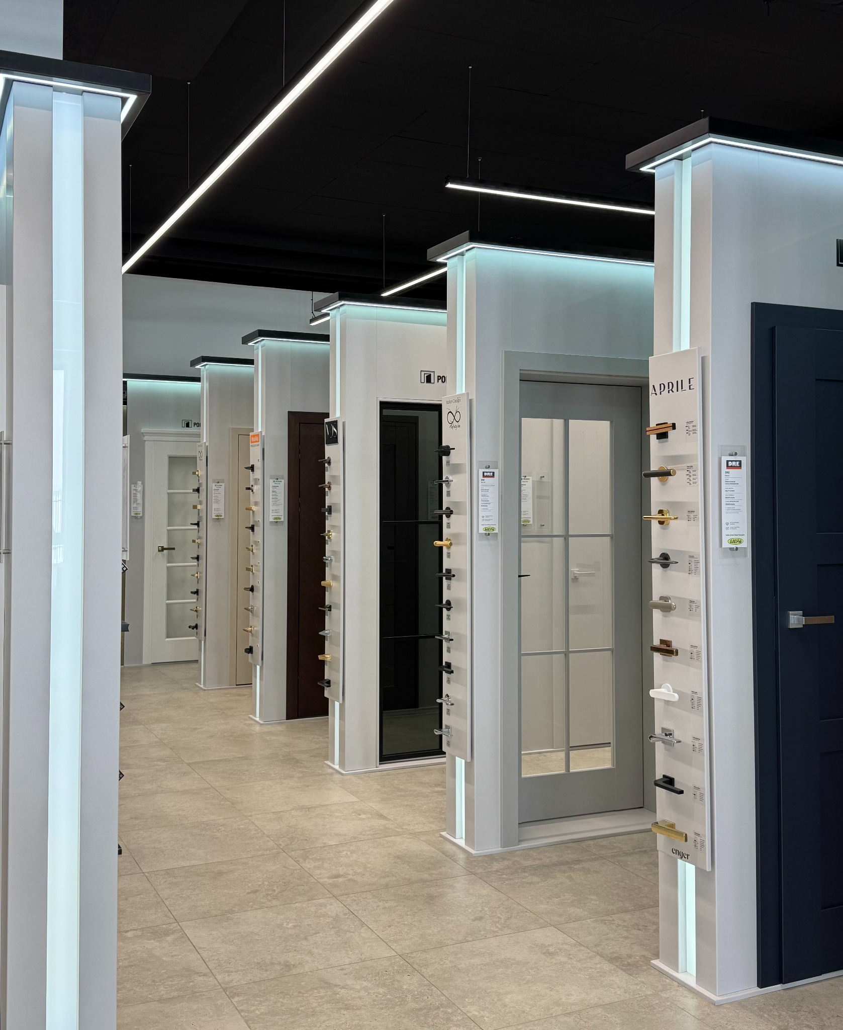 Ekspozycja różnych modeli i kolorów drzwi wewnętrznych w salonie w Rzeszowie. Widoczne próbki klamek i szyldów. Oświetlenie LED podkreśla design.