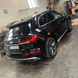 Czarne Audi Q5 po detailingu w warsztacie, widok z tyłu, połysk karoserii, felgi aluminiowe. Warsztat z narzędziami w tle, czysta podłoga.