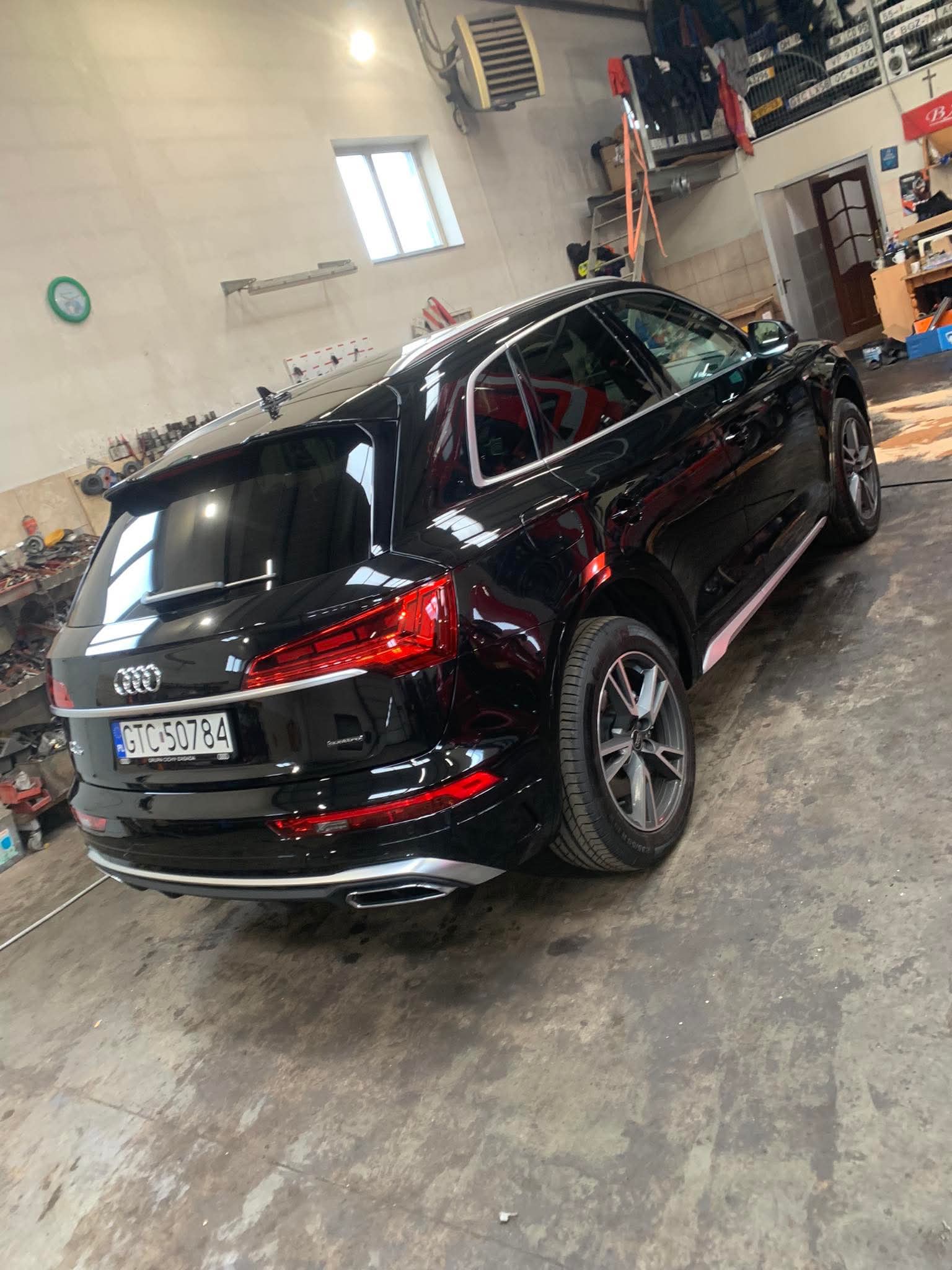 Czarne Audi Q5 po detailingu w warsztacie, widok z tyłu, połysk karoserii, felgi aluminiowe. Warsztat z narzędziami w tle, czysta podłoga.